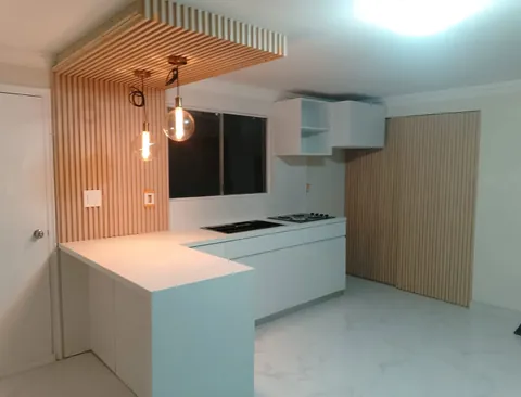 Cocina blanca con barra en cascada y duela de madera en muro y techo