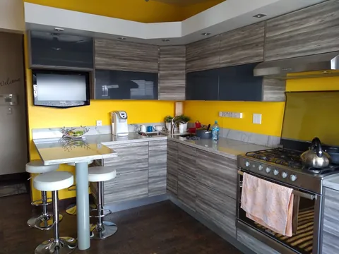 Cocina en L de maderado gris con alacenas de vidrio y barra